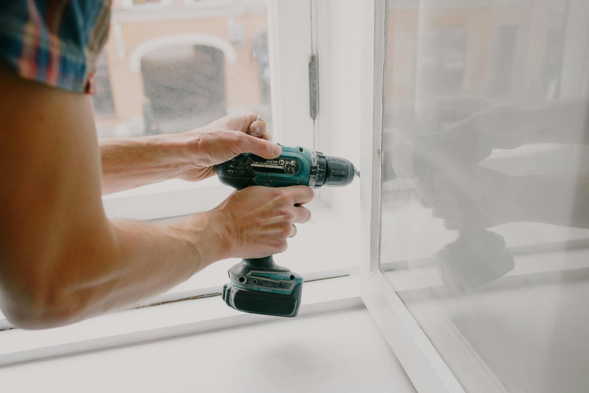 Person using a cordless drill on a window frame