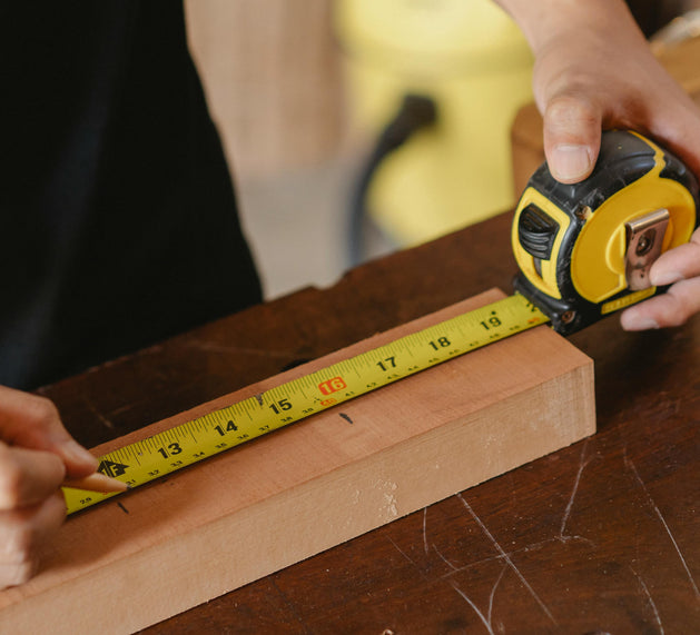 Person measuring a wooden plank with a tape measure on a wooden surface