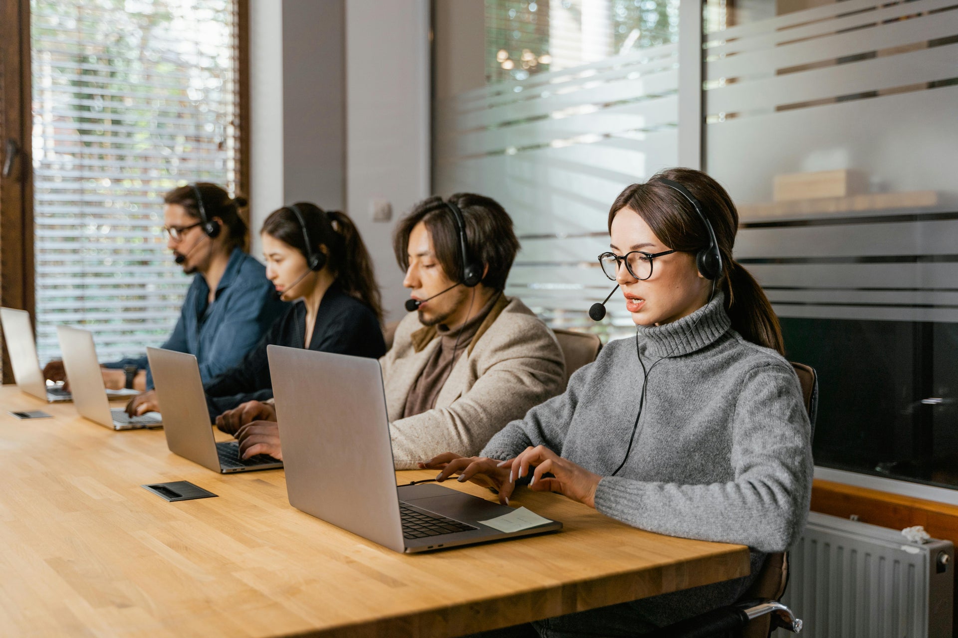 Four call center agents working at a desk with laptops and headsets.