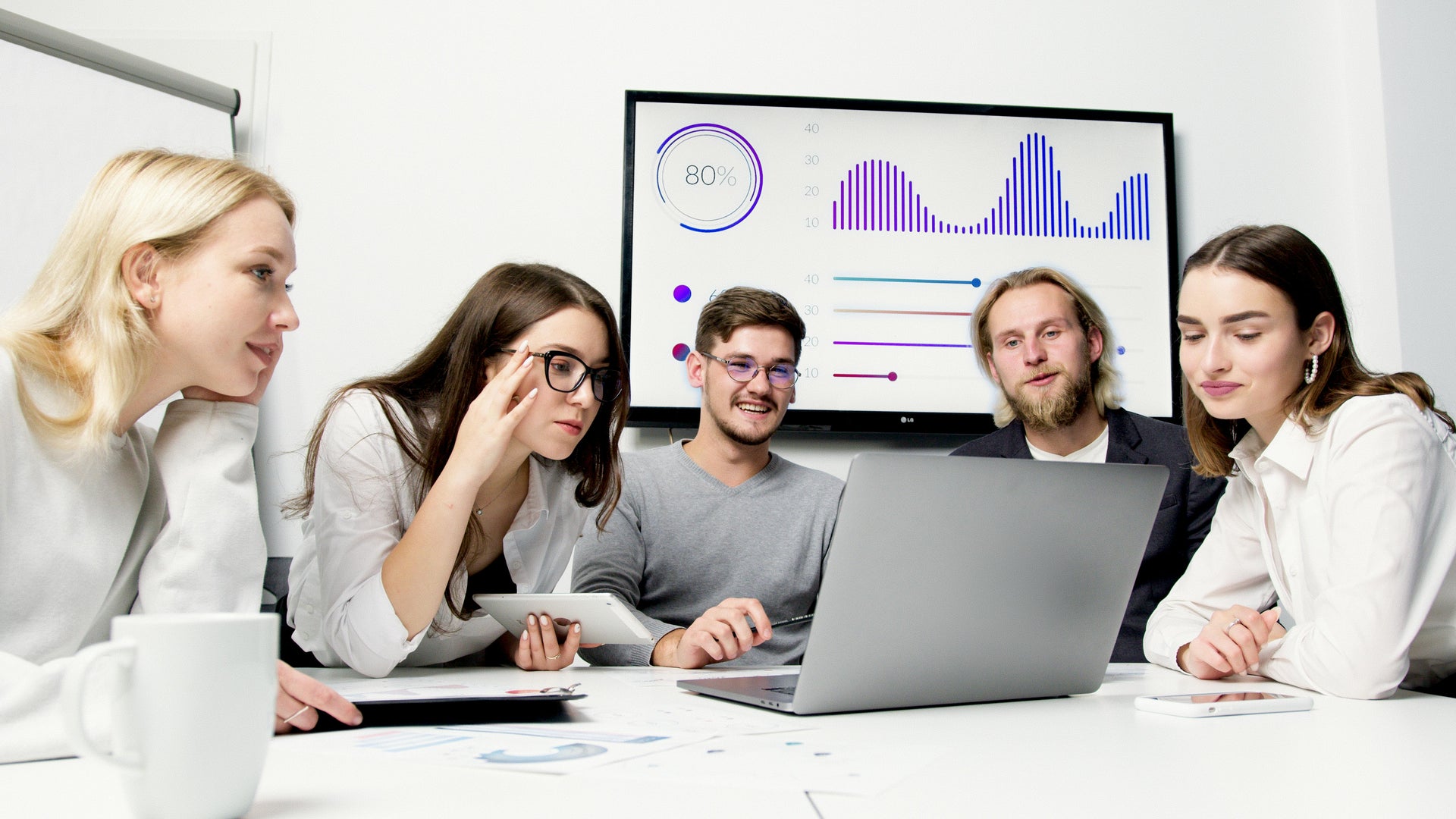 Group of people in a meeting with a screen displaying graphs and data.