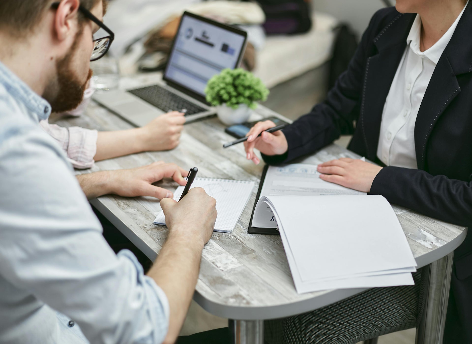 Two people sitting at a table with papers and a laptop, engaged in a discussion.