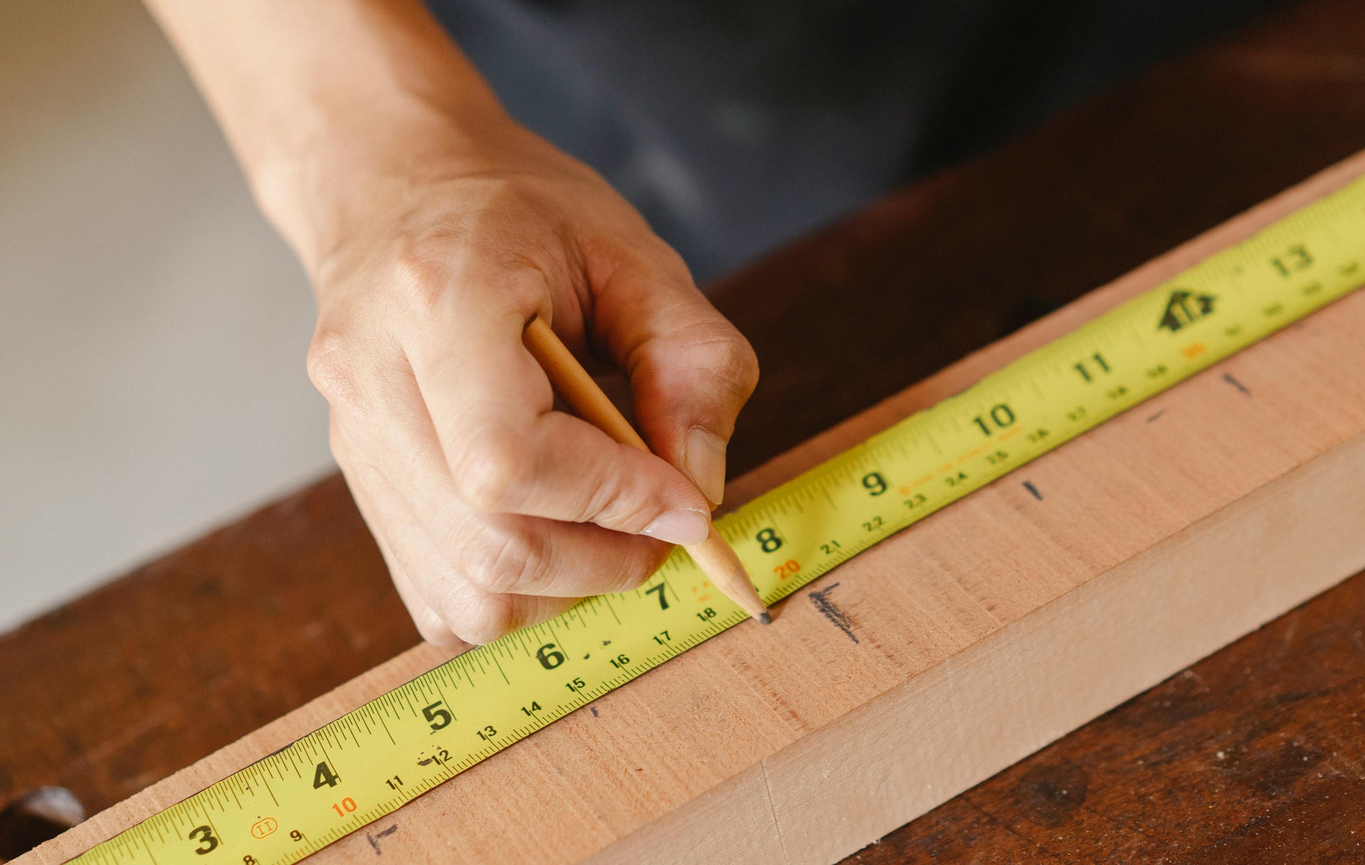 Hand using a yellow measuring tape on a wooden surface