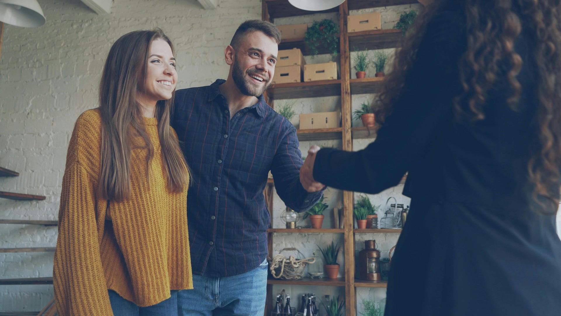 Two people shaking hands in a room with shelves and plants